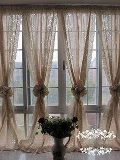 a vase filled with flowers sitting next to two windows covered in sheer curtaines and bowknots