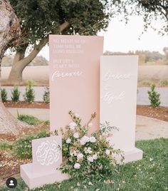 two pink and white signs sitting on top of a grass covered field next to trees