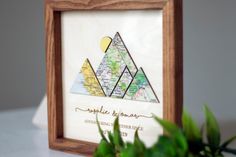 a wooden frame with a map and mountains in the center on a table next to a potted plant