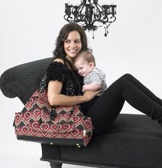 a woman sitting on a couch holding a baby in her lap with a chandelier hanging from the ceiling