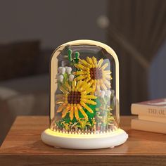 a sunflower under a glass dome on top of a table next to a book