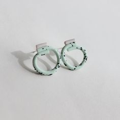 two pairs of earrings sitting on top of a white surface, one with black dots and the other without