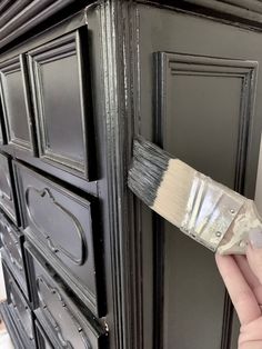 a person holding a paintbrush in front of an old black painted cabinet with drawers