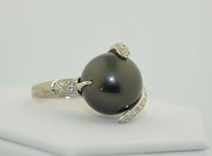 This is an impressively large pearl ring. The pearl is a south Sea Black Tahitian Pearl. The pearl is drilled and mounted with pave diamond accents. The small prong is drilled on the side and the fingers of diamonds are securing the pearl with no movement. This pearl is big, measuring in at 15.5 mm. It is a deep grey/black, perfectly round. There are a couple of natural dimples on the side not the top of the pearl as photographed The setting is 14K White gold, not hallmarked but tested and guara Tahitian Pearl Ring With Diamond Accents Fine Jewelry, Classic Tahitian Pearl Ring With Diamond Accents, Fine Jewelry Tahitian Pearl Ring With Diamond Accents, Luxury Tahitian Pearl Ring With Diamond Accents, Tahitian Pearl Ring With Diamond Accents, Elegant Tahitian Pearl Ring With Diamond Accents, Formal Tahitian Pearl Ring With Diamond Accents, Tahitian Black Pearls, Etsy Gold Ring