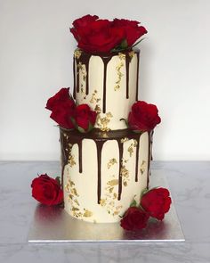 a three tiered cake with chocolate and red roses on the top, sitting on a silver platter