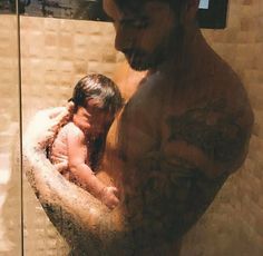 a man holding a baby in his arms while standing next to a glass shower door