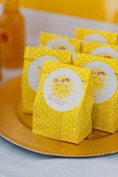 small yellow boxes with sun designs on them sitting on a gold plate next to honey jars