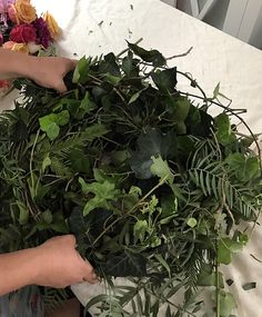 someone is cutting up some green plants on a white tablecloth with flowers in the background