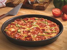 a pizza sitting in a pan on top of a wooden cutting board next to tomatoes