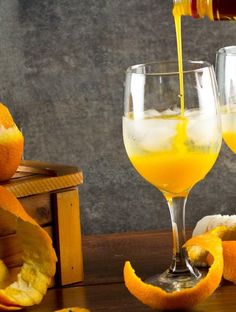 an orange juice being poured into a glass next to sliced oranges on a table