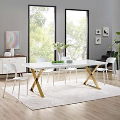 a white dining table with gold cross legs in a modern living room setting by the window