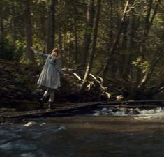 a woman standing on a log in the middle of a river with her arms outstretched