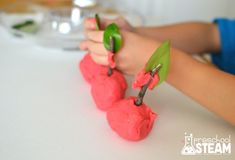 two hands holding green leaves and pink play dough