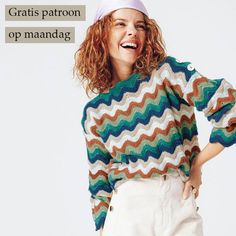 a woman wearing a multicolored sweater and white pants with her hands on her hips