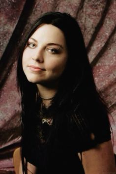 a woman with long black hair sitting in front of a curtain