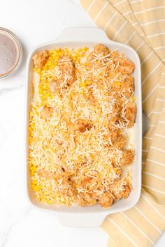 a casserole dish with chicken, corn and cheese next to a cup of sauce