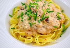 a white plate topped with pasta covered in sauce and green onion sprinkles