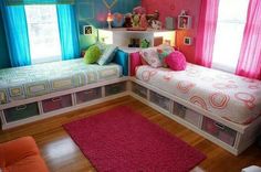 two beds in a room with pink and blue curtains on the windowsills above them