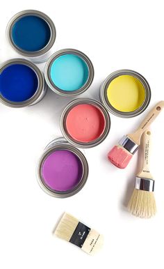 four paint cans with different colored paints and a brush next to them on a white surface