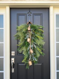 a christmas wreath hanging on the front door with bells and greenery attached to it