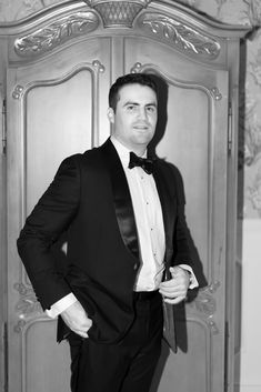 a man in a tuxedo standing next to a wooden door wearing a bow tie