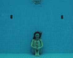 a woman sitting in the middle of a swimming pool with her hands on her hips