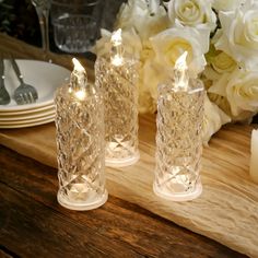 three clear glass candles sitting on top of a wooden table next to flowers and plates