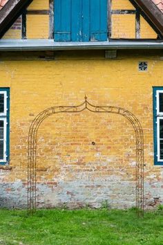 a yellow brick building with blue shutters and an iron arch in front of it