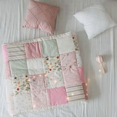 a white bed topped with pink and green patchwork quilted bedspread next to pillows