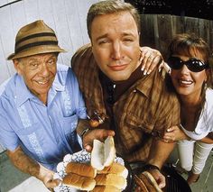 two men and a woman standing next to each other in front of a grill with hot dogs on it