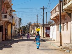 a woman walking down the street in front of some buildings with people on either side