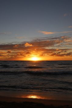 the sun is setting over the ocean with clouds in the sky and water on the beach