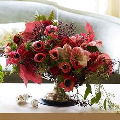 a vase filled with red flowers sitting on top of a wooden table next to a couch