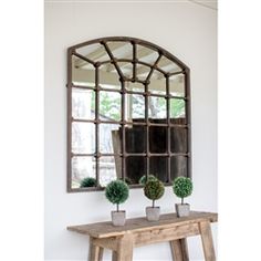 a wooden table topped with potted plants under a large mirror mounted on the wall