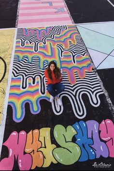 a woman is sitting on the ground in front of some colorful graffiti designs and letters