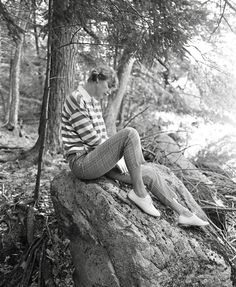 a woman is sitting on a rock in the woods