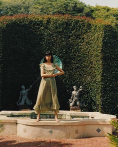 a woman standing in front of a fountain with an umbrella