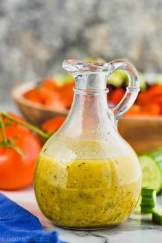 a glass pitcher filled with dressing next to some sliced cucumbers and tomatoes