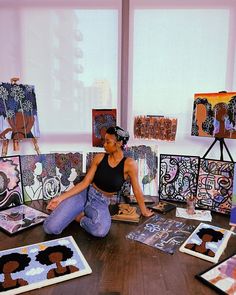 a woman is sitting on the floor in front of some paintings and other art work