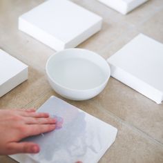 a person's hand on a piece of paper next to a bowl and square object