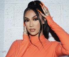 a woman in an orange latex outfit holding her hair