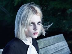 a woman with blonde hair wearing a black shirt and white tie sitting on a park bench