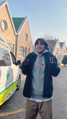 a man standing in front of a van giving the peace sign with both hands and wearing a green and white hoodie