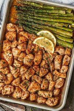 chicken and asparagus in a pan with lemon wedges