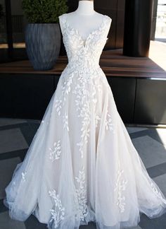 a white wedding dress is on display in front of a large potted plant and window