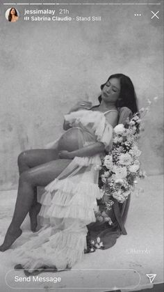 a black and white photo of a woman sitting on a chair with flowers in her lap