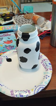 a white and black vase sitting on top of a wooden table next to a plate