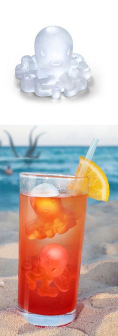 an orange drink sitting on top of a sandy beach next to the ocean with ice cubes