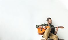 a man sitting on top of a stool holding an acoustic guitar in his right hand