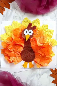 a turkey made out of tissue paper on top of a piece of paper with leaves around it